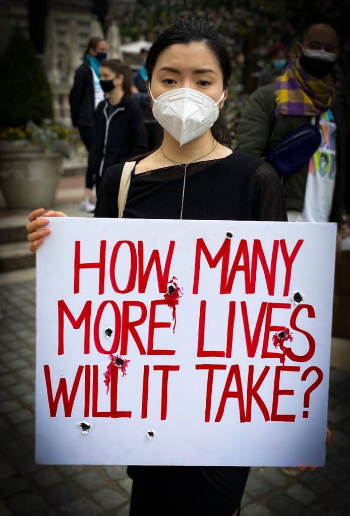 Person wearing mask holding protest sign about pandemic impact.