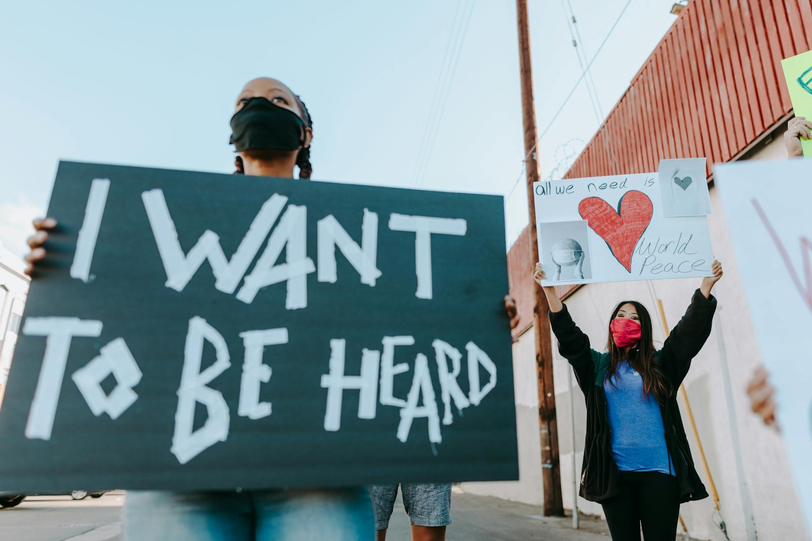 People wearing face masks hold signs at a peaceful outdoor protest.